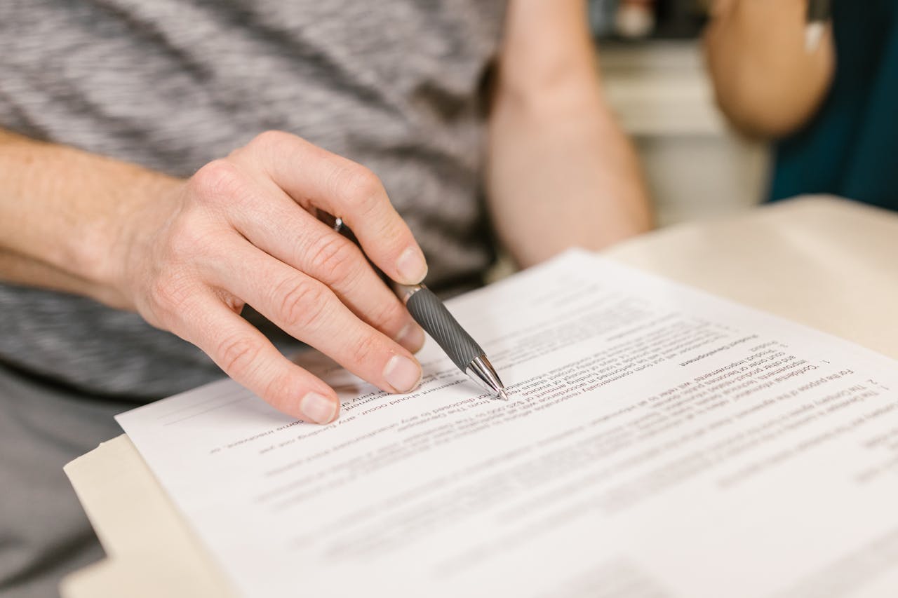 Close-up of a persons hand signing an important legal document with a pen indoors.