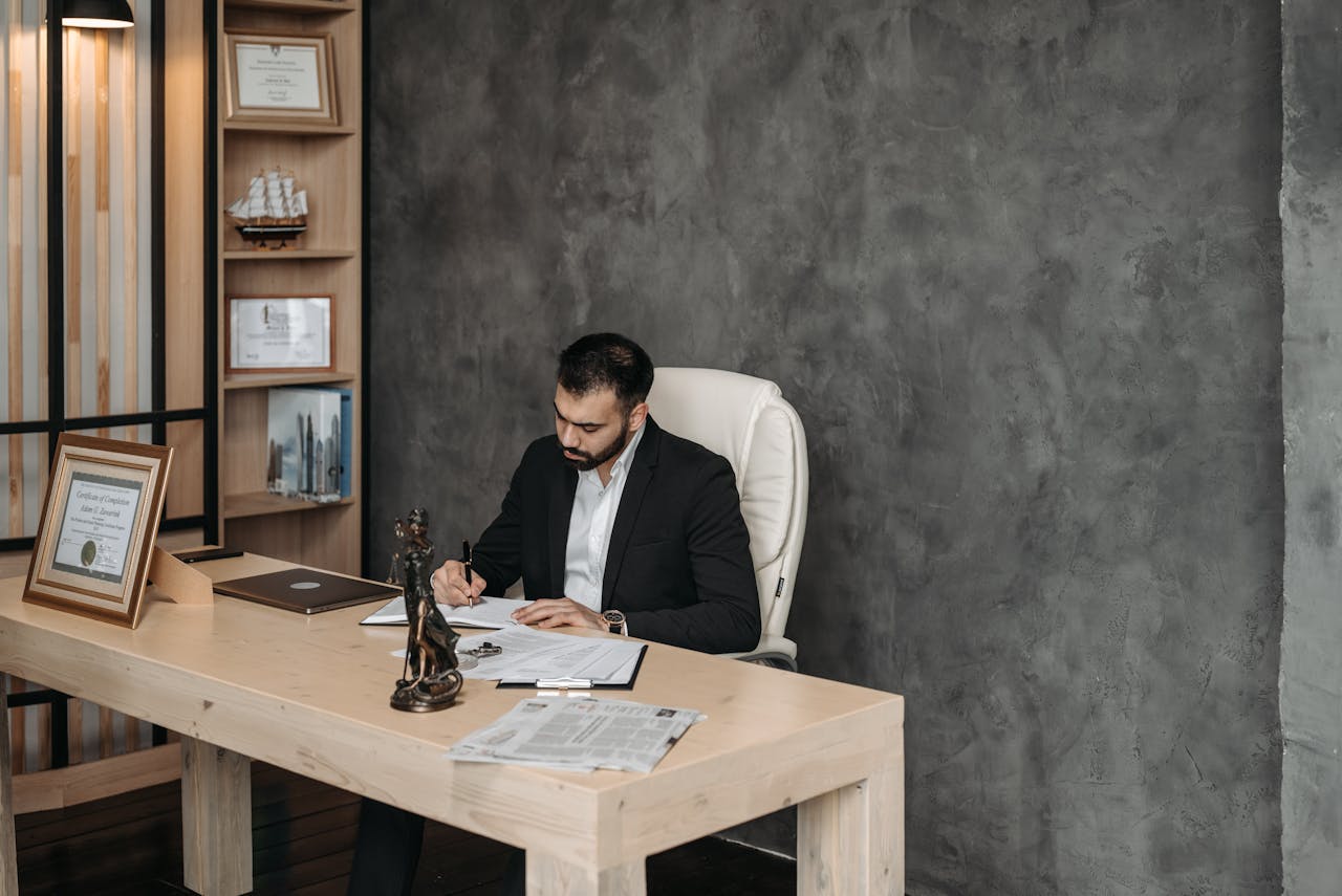 Businessman in a suit writing at a desk in a modern office setting.